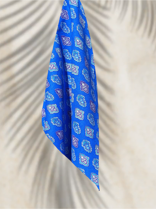 Bandana bleu en coton Valdrôme, suspendu sur fond clair avec ombres de palmiers. Motifs floraux traditionnels, rendu premium et artisanal, produit SouldlroW.