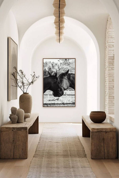 Tirage encadré de chevaux en noir et blanc, présenté dans un couloir voûté avec bancs en bois et vases décoratifs.